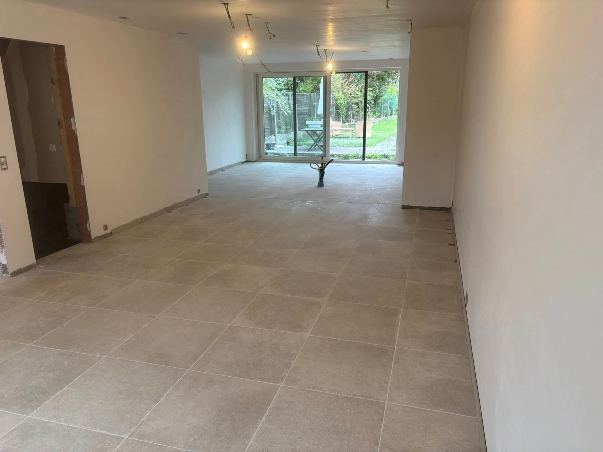 Afgewerkte beige tegelvloer in leefruimte met zicht op tuin